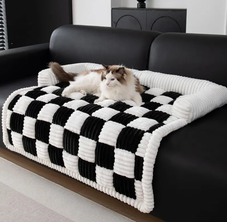 A cat on a black and white checkered pet bed in a living room.